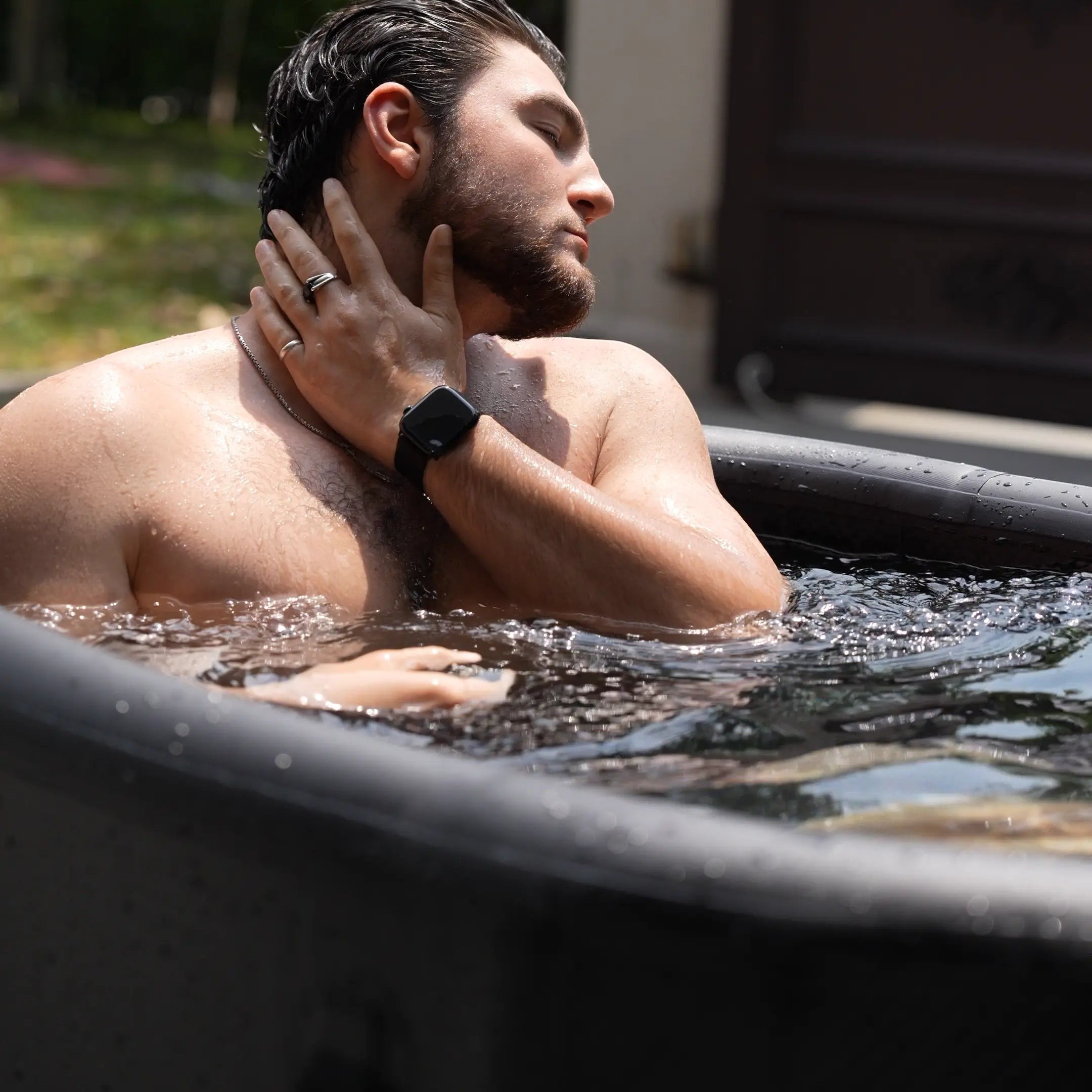 A man is using a Garvnive black PVC ice bath tub for cold therapy recovery; the tub features an air-layered insulation design.