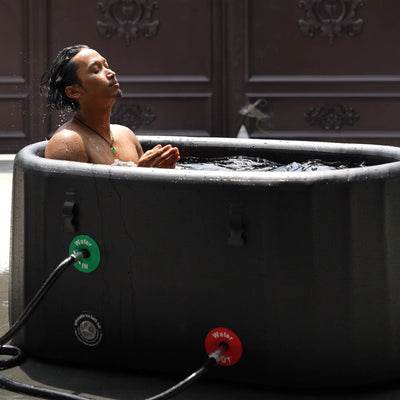 A man is using a Garvnive black PVC ice bath tub for cold therapy recovery; the tub features an air-layered insulation design.
